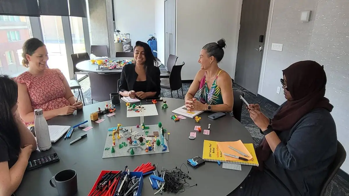 Four participants around a table with a LEGO Serious Play landscape build during the July Ottawa cohort